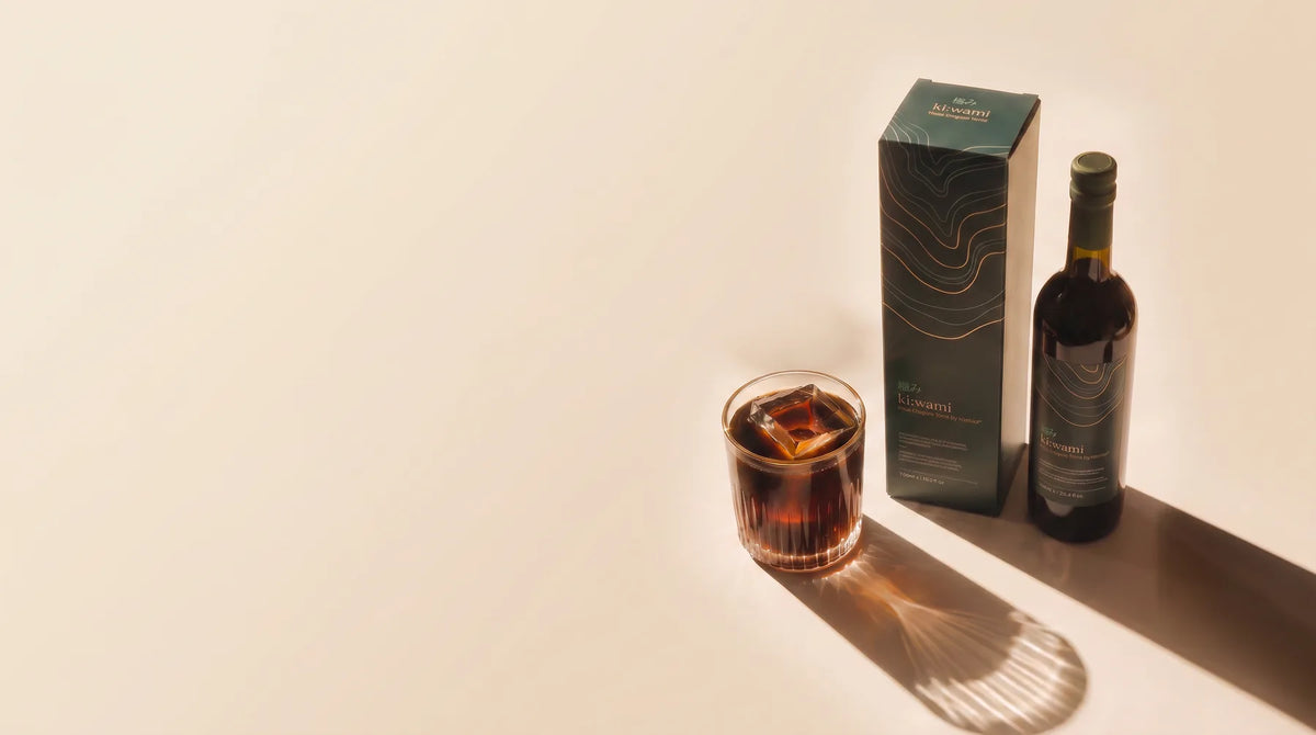ki:wami bottle and carton beside a glass of amber elixir on a warm cream surface