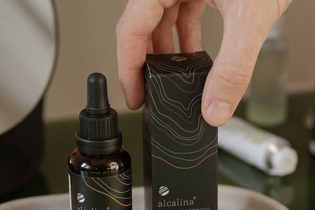 A hand setting an alcalina bottle and its carton on a bathroom shelf
