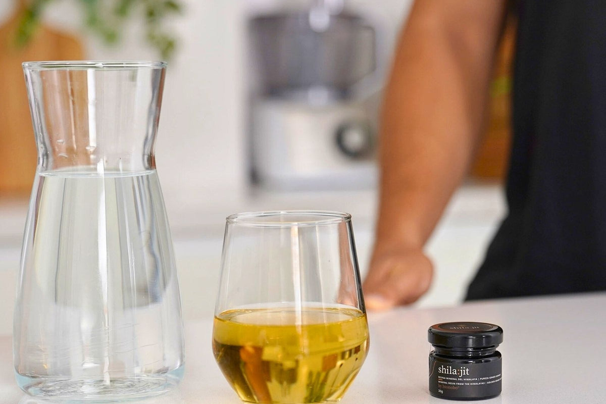 A water carafe, a glass and a jar of shila:jit dorado on a kitchen counter